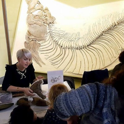 Ashley shows fossils to CMNH guests while a giant Xiphactinus looms in the background.