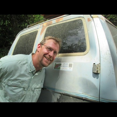 Ed striking a pose beside an Greg Carr's truck with an outdated Saber Tooth Salmon sticker. Greg Carr&rsquo;s the NARG amateur paleontologist who helped excavate the giant salmon! Ed was posing with that bumper sticker on the very trip when the new skulls were found.