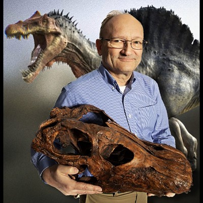 Hans Sues holding an Apatosaurus skull cast as a Spinosaurus lurks menancingly in the background.&nbsp;