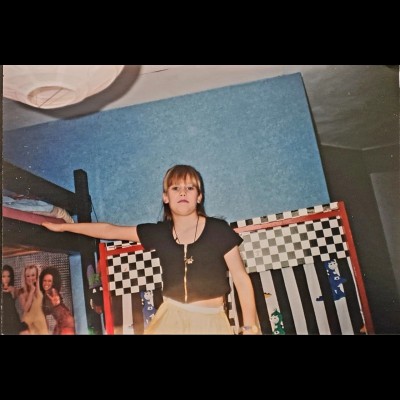 Melanie aged ~10 years old, in her bedroom with her little dinosaur-theater decor in the background - and of course a Spice Girls poster.